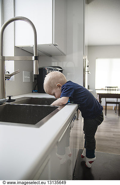 Side view of boy standing on stool by sink in kitchen