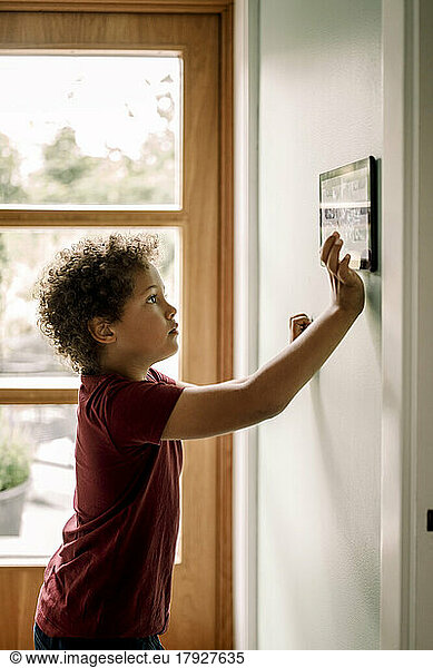 Side view of boy using home automation through tablet PC mounted on wall