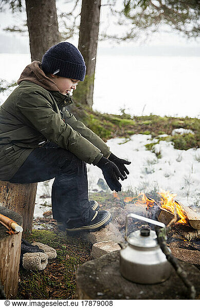Side view of boy warming hands while sitting by bonfire in winter