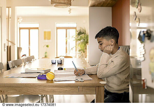Side view of boy writing in book over table at home