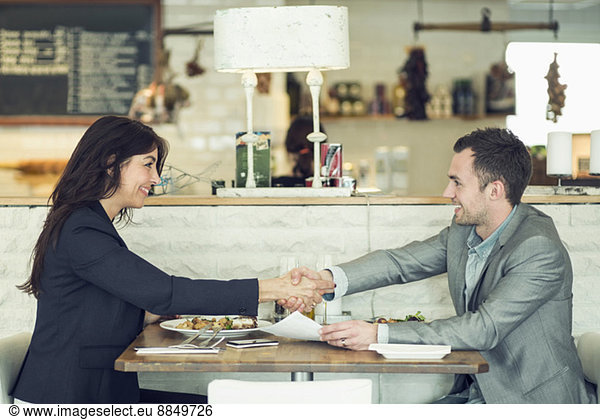 Side view of businessman and businesswoman shaking hands at restaurant table
