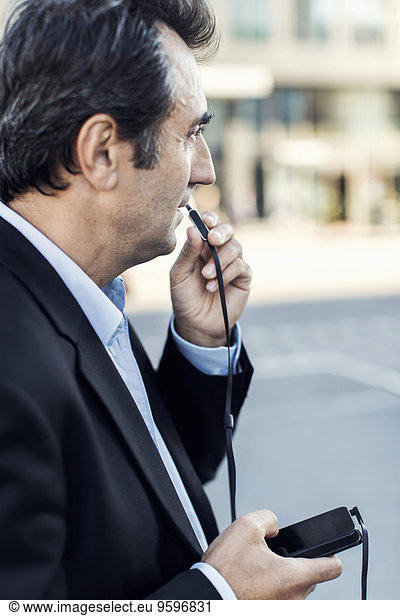 Side view of businessman communicating through headphones using mobile phone on street
