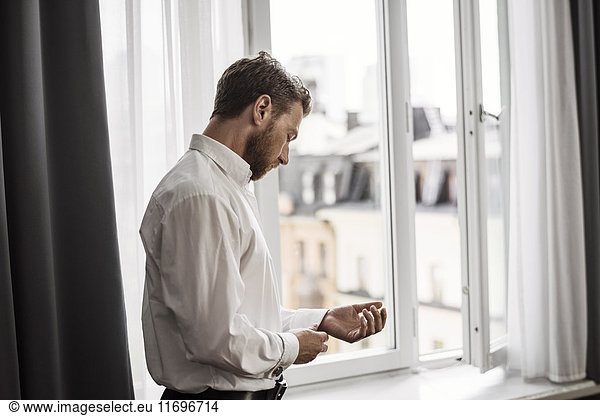Side view of businessman getting dressed against window at hotel room