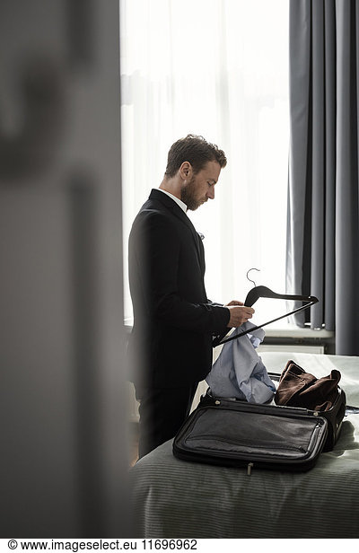 Side view of businessman positioning shirt on coathanger in hotel room