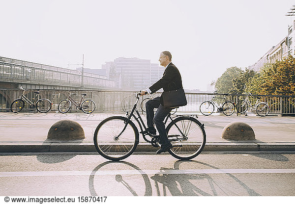 Side view of businessman riding bicycle on road in city against sky