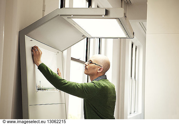 Side view of businessman sticking document on board in office