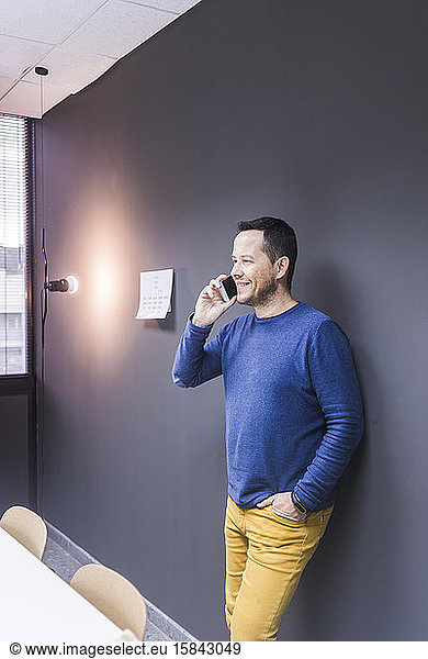 Side view of businessman talking on smart phone while standing against office wall