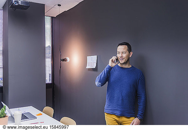 Side view of businessman talking on smart phone while standing against office wall