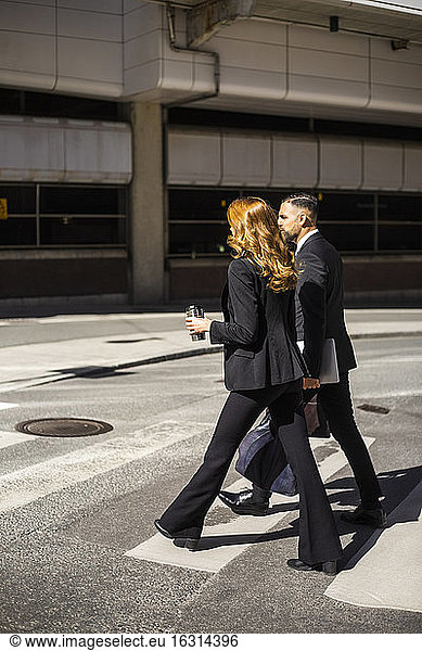 Side view of businesswoman and businessman crossing road in city