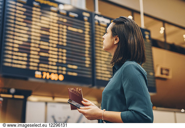Side view of businesswoman looking at arrival departure board in airport