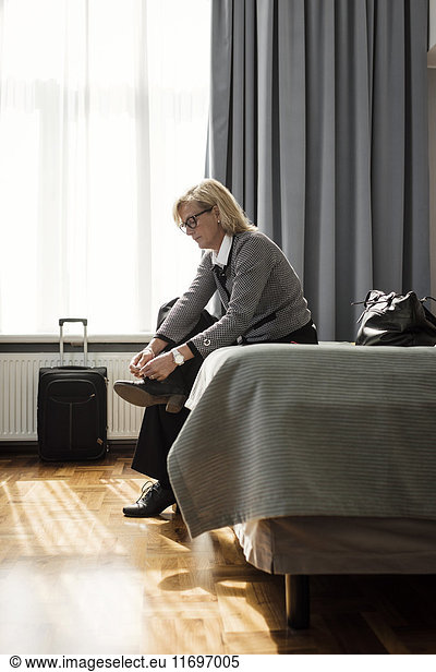 Side view of businesswoman tying shoelace sitting on bed at hotel room