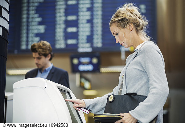 Side view of businesswoman using check in machine at airport