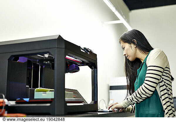 Side view of businesswoman using laptop computer by 3D printer on table in office