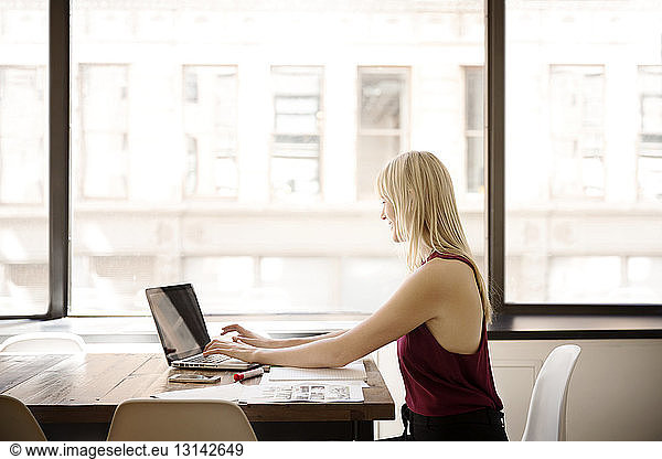 Side view of businesswoman using laptop in creative office