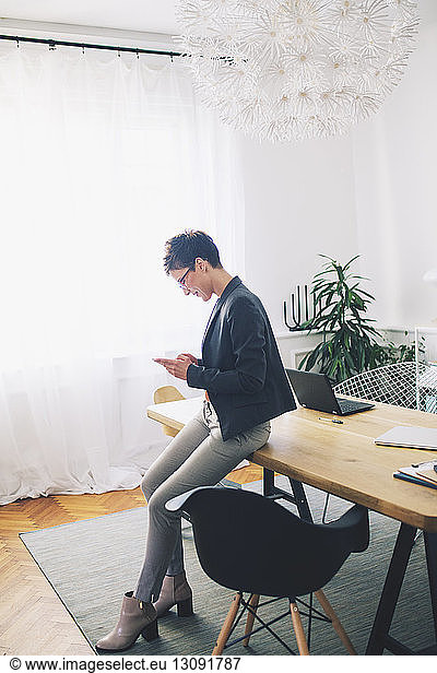 Side view of businesswoman using mobile phone at table in office