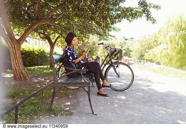 Side view of businesswoman using smart phone while sitting on park bench