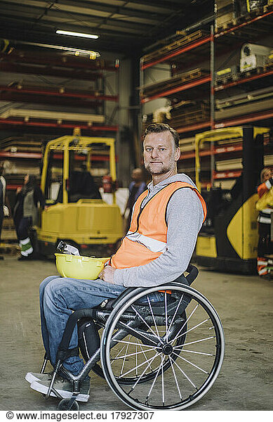 Side view of carpenter with hardhat sitting on wheelchair in warehouse