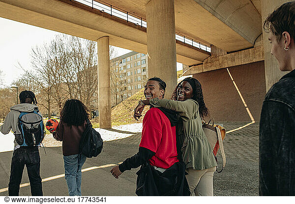 Side view of cheerful multiracial friends walking together below bridge
