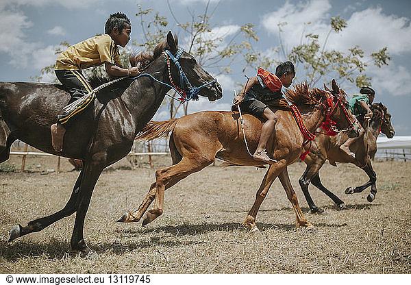 Side view of children riding racehorses during horse racing