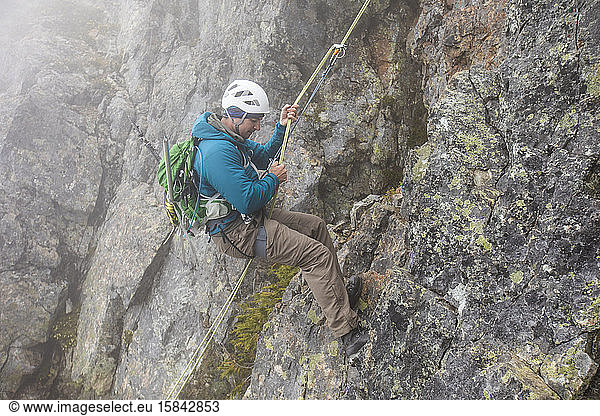 Side view of climber rappelling rocky mountain.