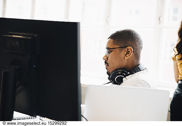 Side view of computer programmer with headphones sitting against window in office