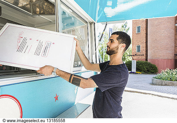 Side view of confident young male salesman holding menu placard at food truck