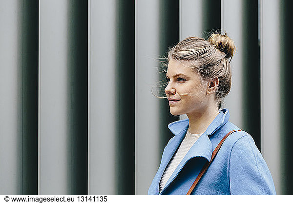 Side view of confident young woman wearing trench coat against shutter in city