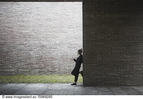 Side view of contemplating woman standing by wall