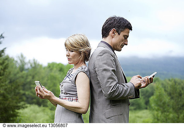 Side view of couple using mobile phone while standing against sky
