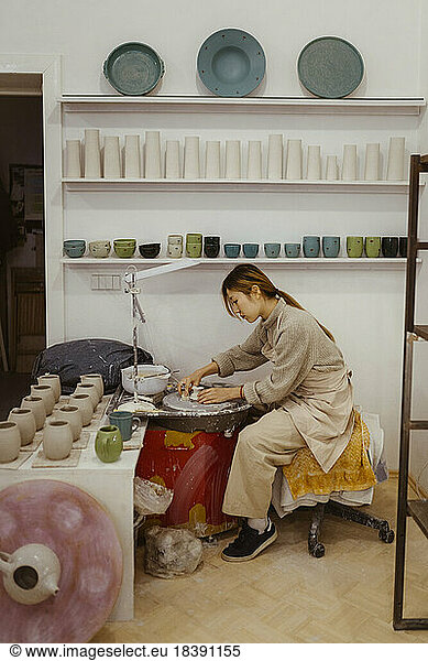 Side view of craftswoman working on pottery wheel at workshop