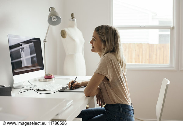 Side view of creative female designer using graphics tablet at home