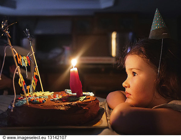 Side view of cute girl looking at birthday cake on table in darkroom