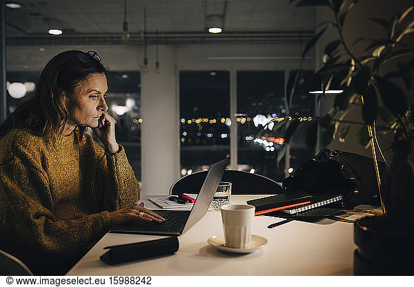 Side view of dedicated mature businesswoman using laptop while working late at creative office