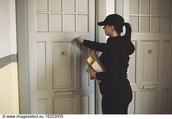 Side view of delivery woman with package knocking at door