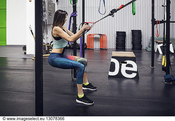 Side view of determined female athlete pulling suspension belts at gym