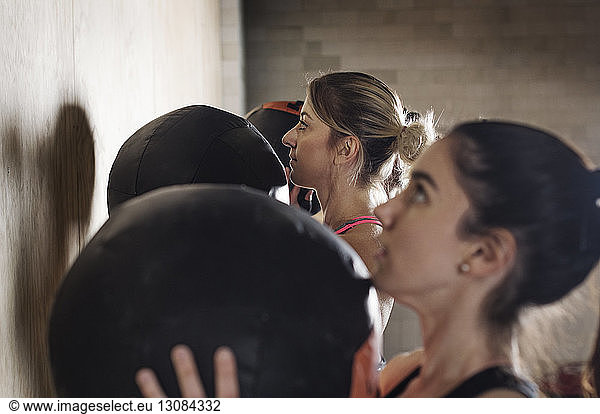 Side view of determined sportswomen exercising with medicine balls in gym