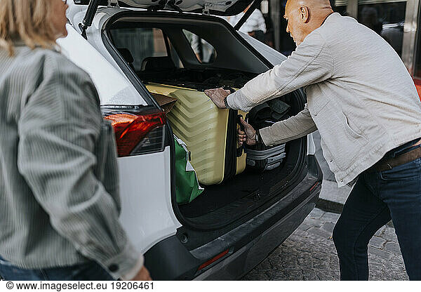 Side view of elderly man loading suitcase in car trunk