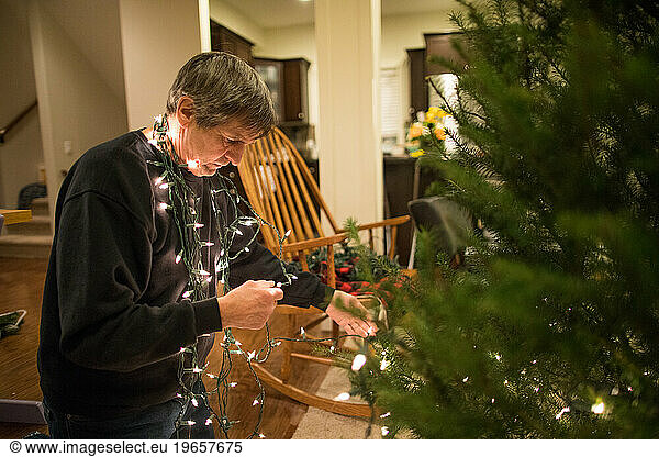 side view of Elderly man stringing lights on the tree.