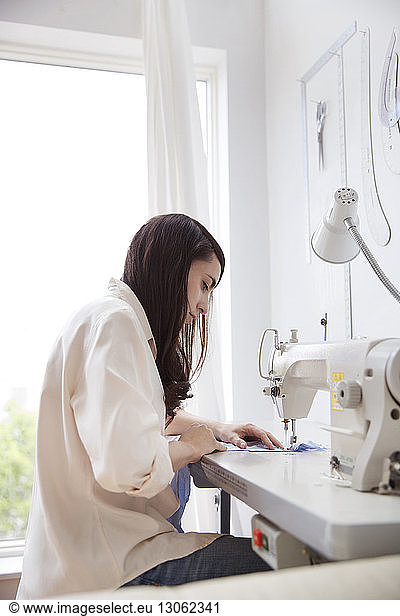 Side view of fashion designer using sewing machine in studio