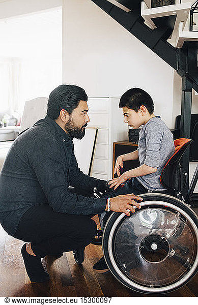 Side view of father looking at autistic son sitting on wheelchair at home