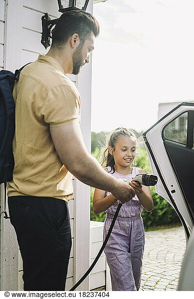 Side view of father teaching daughter to charge electric car