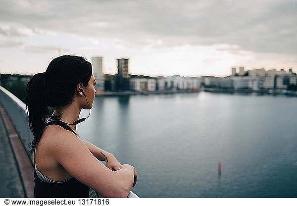 Side view of female athlete looking at city while standing on footbridge over sea