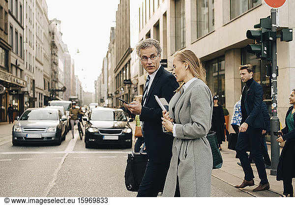 Side view of female business person with male coworker crossing road in city
