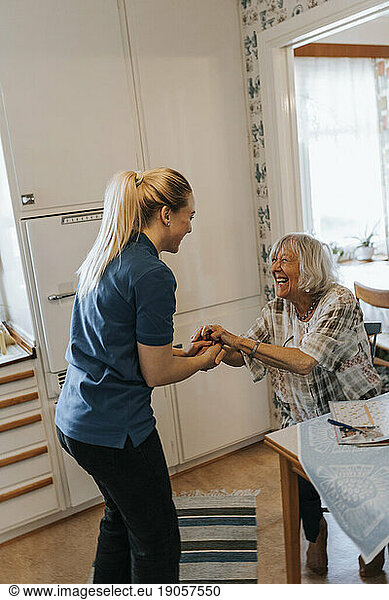 Side view of female caregiver holding hands while talking with senior woman at home