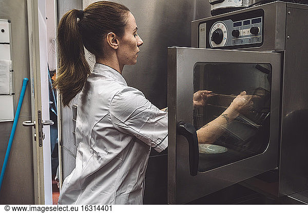 Side view of female chef putting dish in oven at commercial kitchen