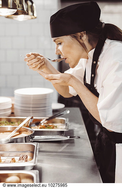 Side view of female chef tasting food at commercial kitchen