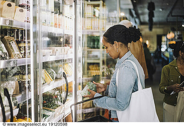 Side view of female customer examining broccoli at organic delicatessen