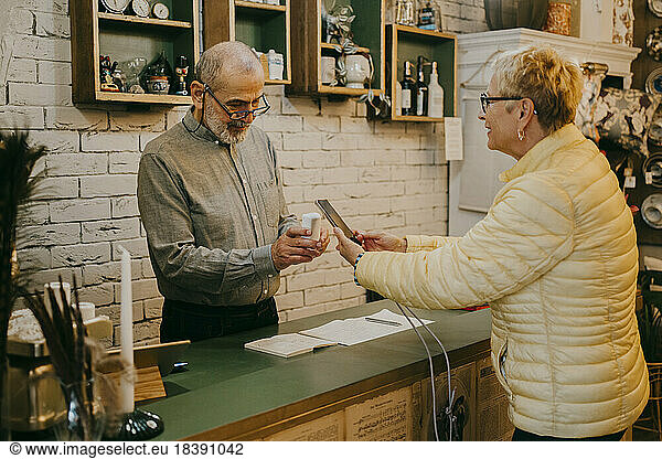 Side view of female customer paying via tap to pay method after shopping at interior store