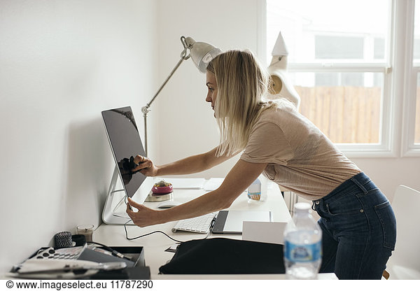 Side view of female graphic designer touching desktop monitor at home