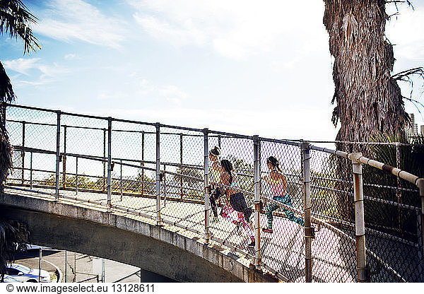 Side view of female joggers on bridge against sky